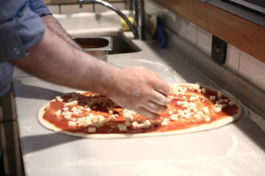 Pizza şefi ticari bir mutfakta sosu tabana koydu.