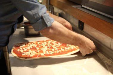 Pizza şefi ticari bir mutfakta sosu tabana koydu.