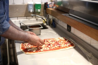 Pizza şefi ticari bir mutfakta sosu tabana koydu.