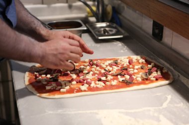 Pizza şefi ticari bir mutfakta sosu tabana koydu.