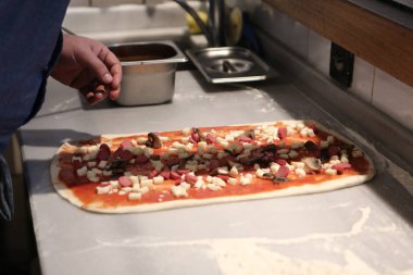 Pizza şefi ticari bir mutfakta sosu tabana koydu.