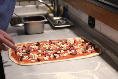 Pizza şefi ticari bir mutfakta sosu tabana koydu.