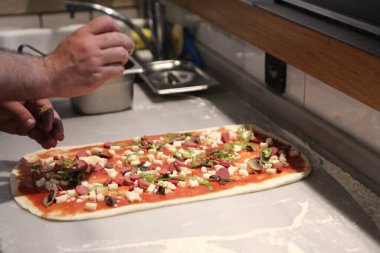 Pizza şefi ticari bir mutfakta sosu tabana koydu.