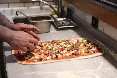 Pizza şefi ticari bir mutfakta sosu tabana koydu.