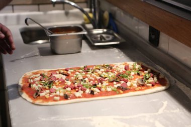 Pizza şefi ticari bir mutfakta sosu tabana koydu.