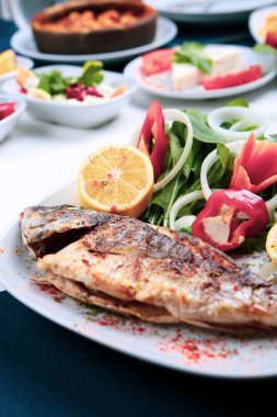 Kızarmış deniz çerezi (cupra) beyaz tabakta soğan, bahçe roketi ve limon dilimli balık.