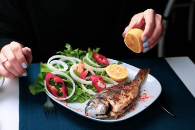 Kızarmış deniz çerezi (cupra) beyaz tabakta soğan, bahçe roketi ve limon dilimli balık.