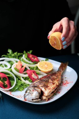 Kızarmış deniz çerezi (cupra) beyaz tabakta soğan, bahçe roketi ve limon dilimli balık.