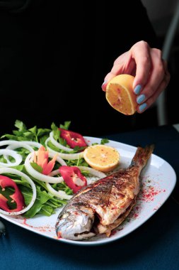 Kızarmış deniz çerezi (cupra) beyaz tabakta soğan, bahçe roketi ve limon dilimli balık.