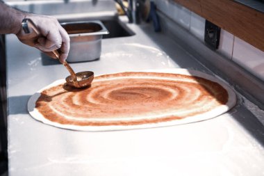 Pizza şefi ticari bir mutfakta sosu tabana koydu.