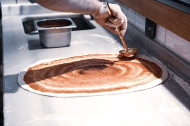 Pizza şefi ticari bir mutfakta sosu tabana koydu.