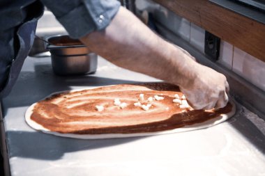 Pizza şefi ticari bir mutfakta sosu tabana koydu.