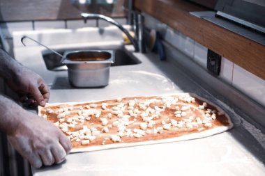 Pizza şefi ticari bir mutfakta sosu tabana koydu.