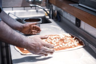 Pizza şefi ticari bir mutfakta sosu tabana koydu.