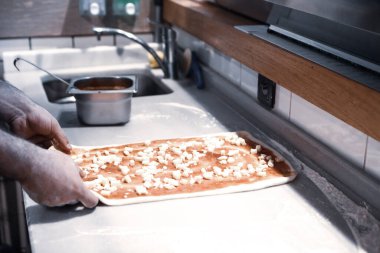 Pizza şefi ticari bir mutfakta sosu tabana koydu.