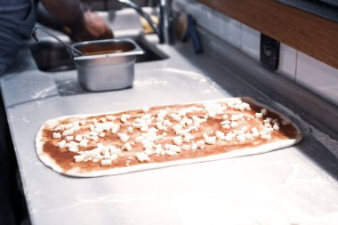 Pizza şefi ticari bir mutfakta sosu tabana koydu.