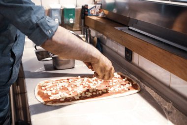 Pizza şefi ticari bir mutfakta sosu tabana koydu.