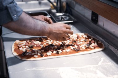 Pizza şefi ticari bir mutfakta sosu tabana koydu.