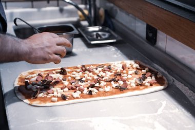 Pizza şefi ticari bir mutfakta sosu tabana koydu.