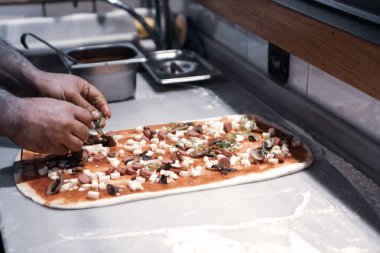 Pizza şefi ticari bir mutfakta sosu tabana koydu.