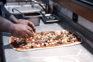 Pizza şefi ticari bir mutfakta sosu tabana koydu.