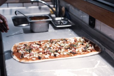 Pizza şefi ticari bir mutfakta sosu tabana koydu.