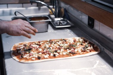 Pizza şefi ticari bir mutfakta sosu tabana koydu.