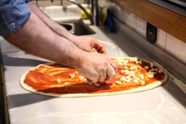 Pizza şefi ticari bir mutfakta sosu tabana koydu.