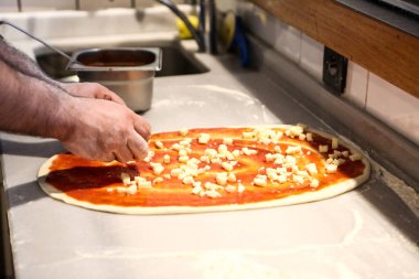 Pizza şefi ticari bir mutfakta sosu tabana koydu.