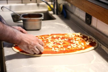 Pizza şefi ticari bir mutfakta sosu tabana koydu.