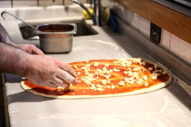 Pizza şefi ticari bir mutfakta sosu tabana koydu.