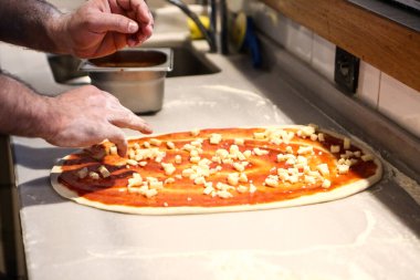 Pizza şefi ticari bir mutfakta sosu tabana koydu.