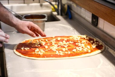 Pizza şefi ticari bir mutfakta sosu tabana koydu.