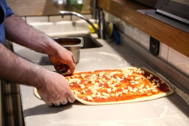 Pizza şefi ticari bir mutfakta sosu tabana koydu.