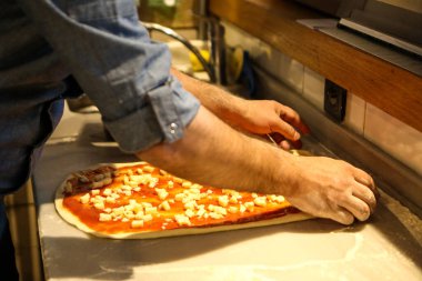 Pizza şefi ticari bir mutfakta sosu tabana koydu.