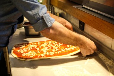 Pizza şefi ticari bir mutfakta sosu tabana koydu.
