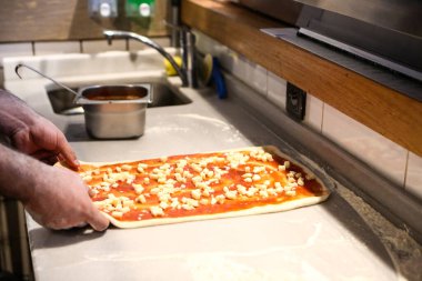 Pizza şefi ticari bir mutfakta sosu tabana koydu.