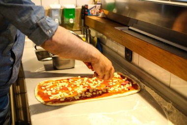 Pizza şefi ticari bir mutfakta sosu tabana koydu.