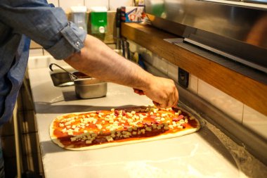 Pizza şefi ticari bir mutfakta sosu tabana koydu.
