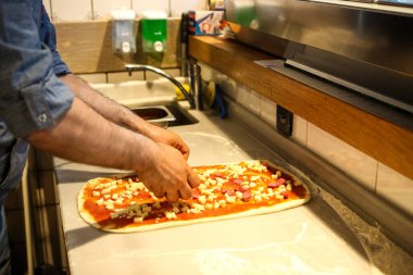 Pizza şefi ticari bir mutfakta sosu tabana koydu.