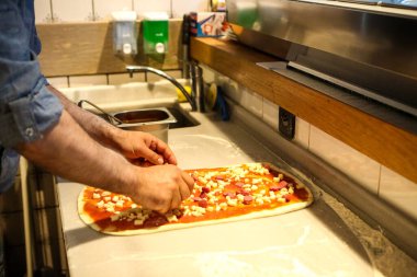 Pizza şefi ticari bir mutfakta sosu tabana koydu.