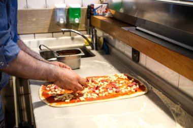 Pizza şefi ticari bir mutfakta sosu tabana koydu.