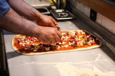 Pizza şefi ticari bir mutfakta sosu tabana koydu.