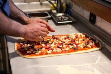 Pizza şefi ticari bir mutfakta sosu tabana koydu.