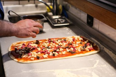 Pizza şefi ticari bir mutfakta sosu tabana koydu.