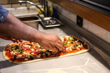 Pizza şefi ticari bir mutfakta sosu tabana koydu.