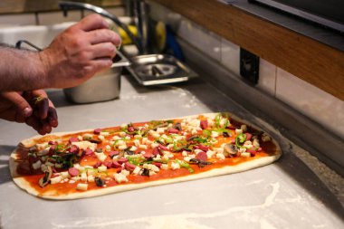 Pizza şefi ticari bir mutfakta sosu tabana koydu.