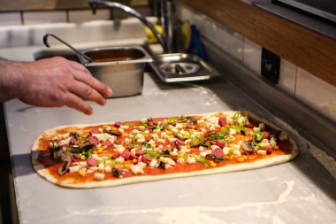 Pizza şefi ticari bir mutfakta sosu tabana koydu.