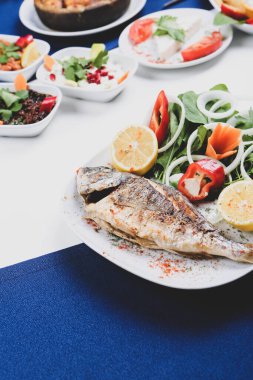 Kızarmış deniz çerezi (cupra) beyaz tabakta soğan, bahçe roketi ve limon dilimli balık.