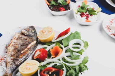 Kızarmış deniz çerezi (cupra) beyaz tabakta soğan, bahçe roketi ve limon dilimli balık.